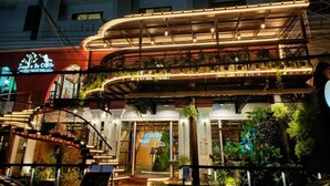 Un edificio de varios pisos con un diseño moderno, que presenta un nivel superior curvo con plantas y un letrero que dice 'Jungle De Cafe'.
