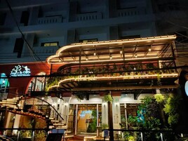 Un immeuble à étages doté d’une architecture moderne, avec un niveau supérieur incurvé agrémenté de plantes et d’une enseigne indiquant « Jungle De Cafe ».