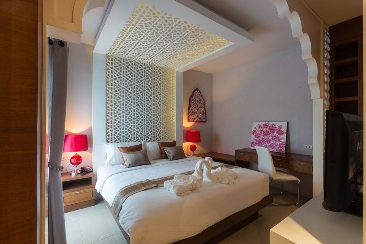 A modern hotel room with a large bed, decorative wall panels, and a red lamp on the nightstand.
