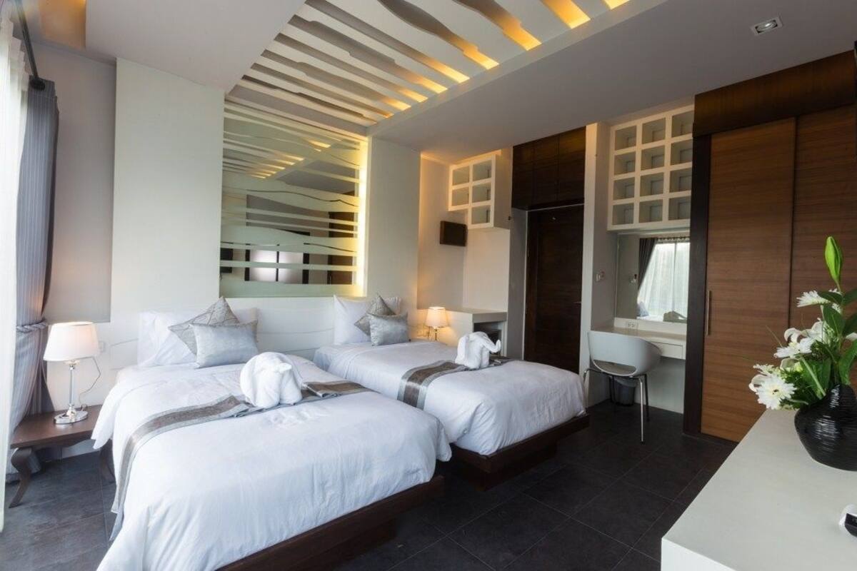 A modern hotel room with two beds, a bathroom, and a seating area.