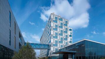 Een modern gebouw met een glazen gevel, een voetgangersbrug en een verzorgd gazon.
