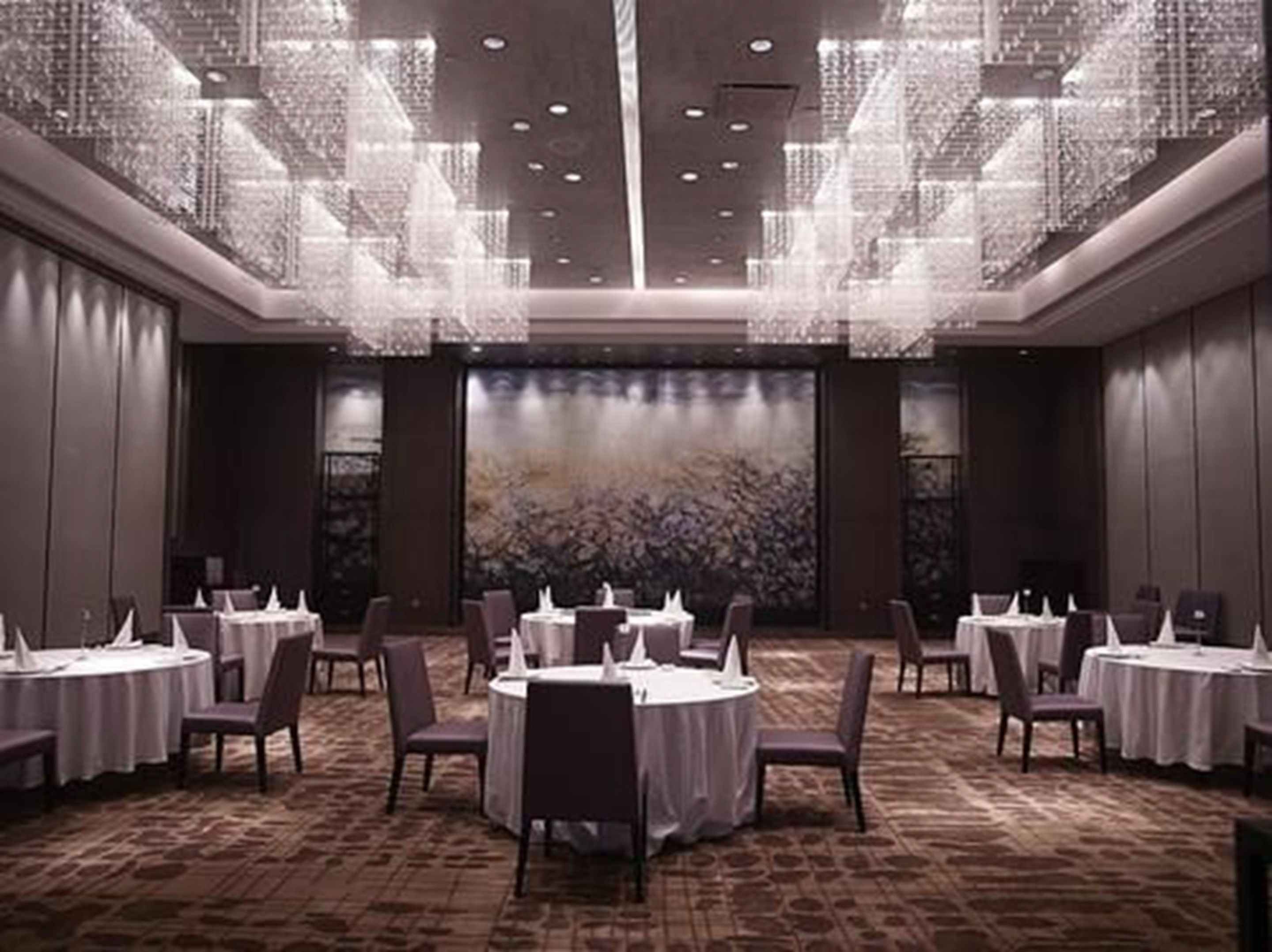 A formal dining area with round tables, chairs, and a chandelier.
