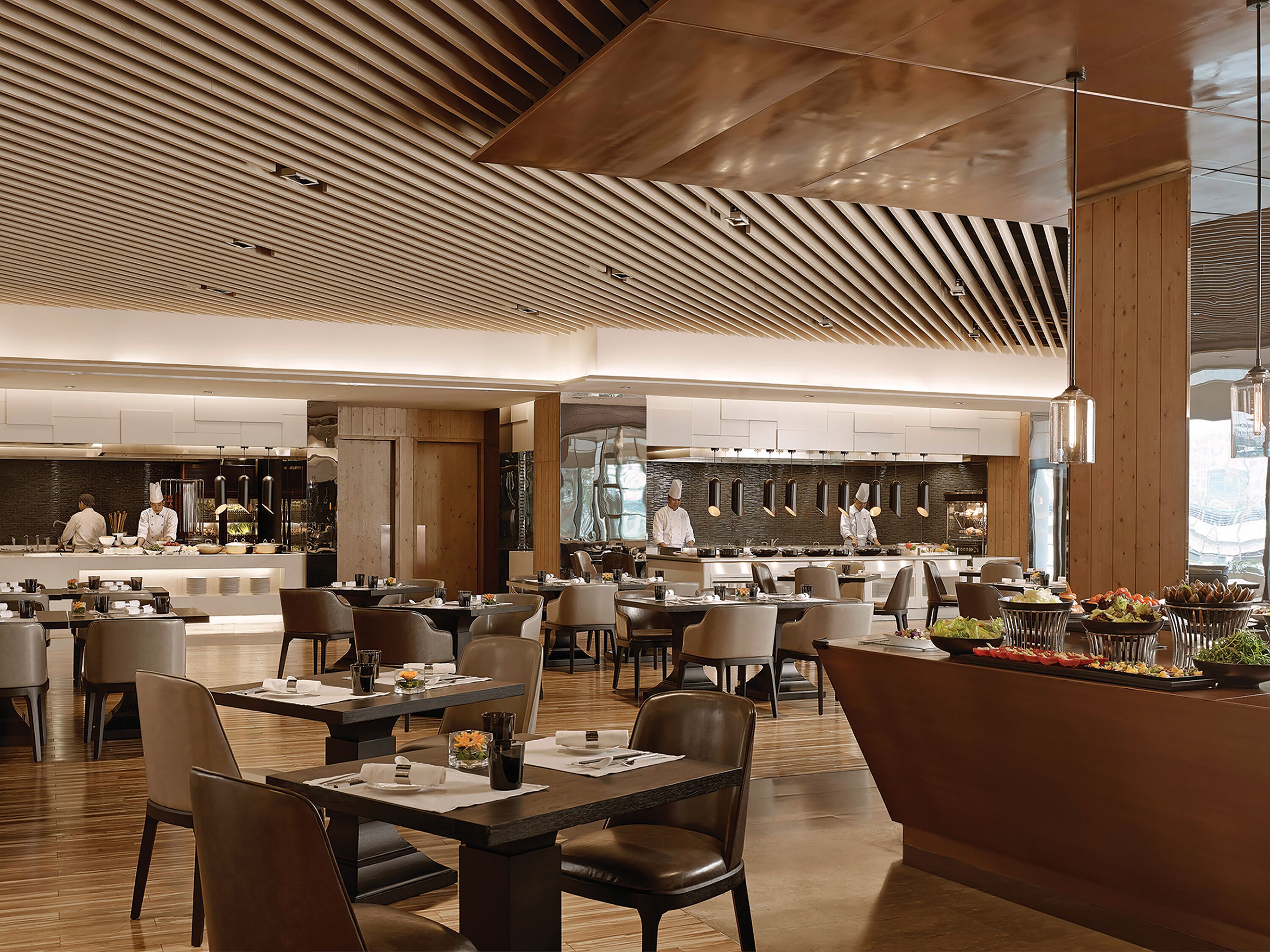 A spacious restaurant with a modern design, featuring a wooden ceiling and a central kitchen area.