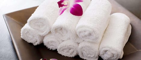 A set of neatly rolled white towels on a square tray with a purple orchid.