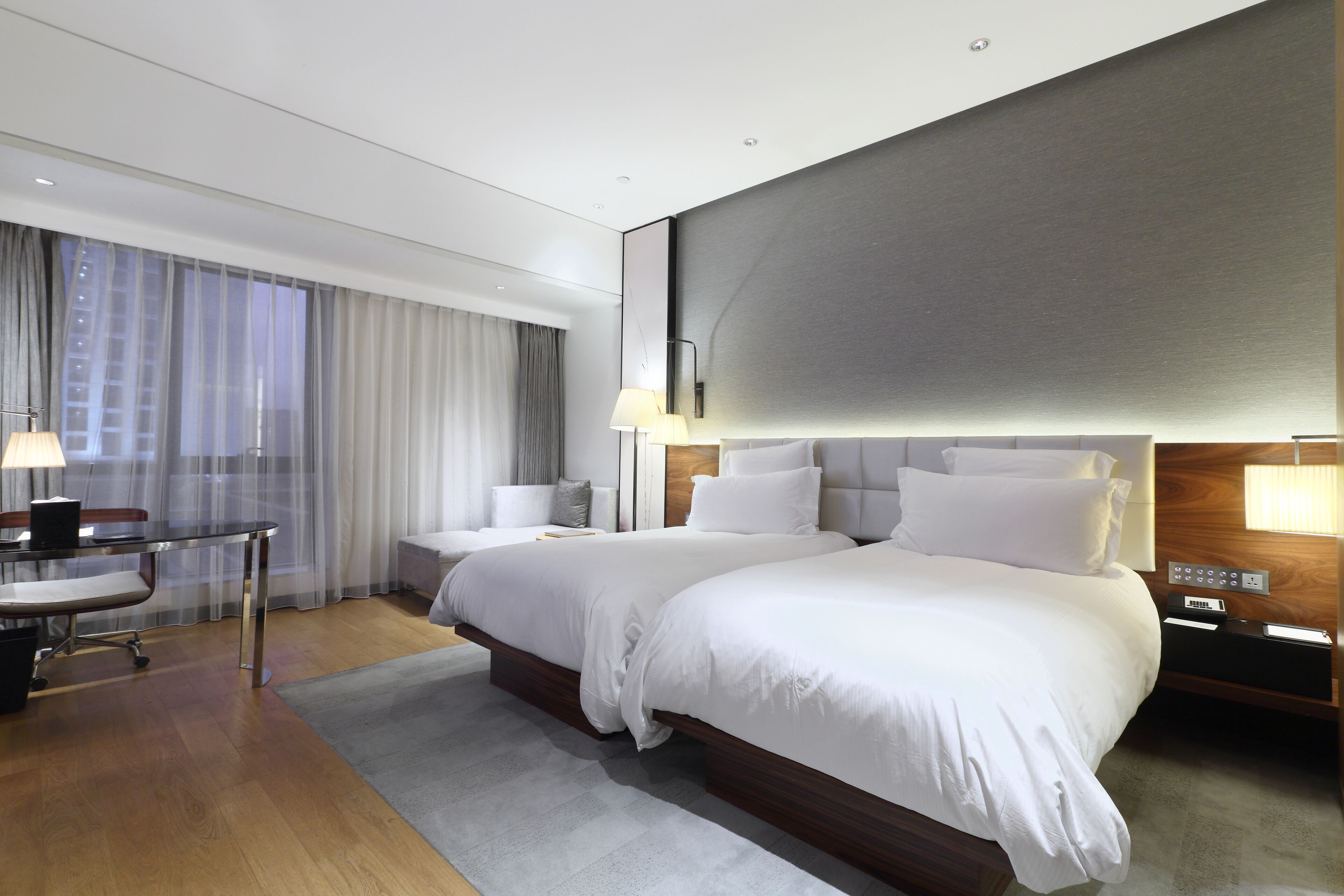 A modern hotel room with two beds, a desk, and a large window with curtains.