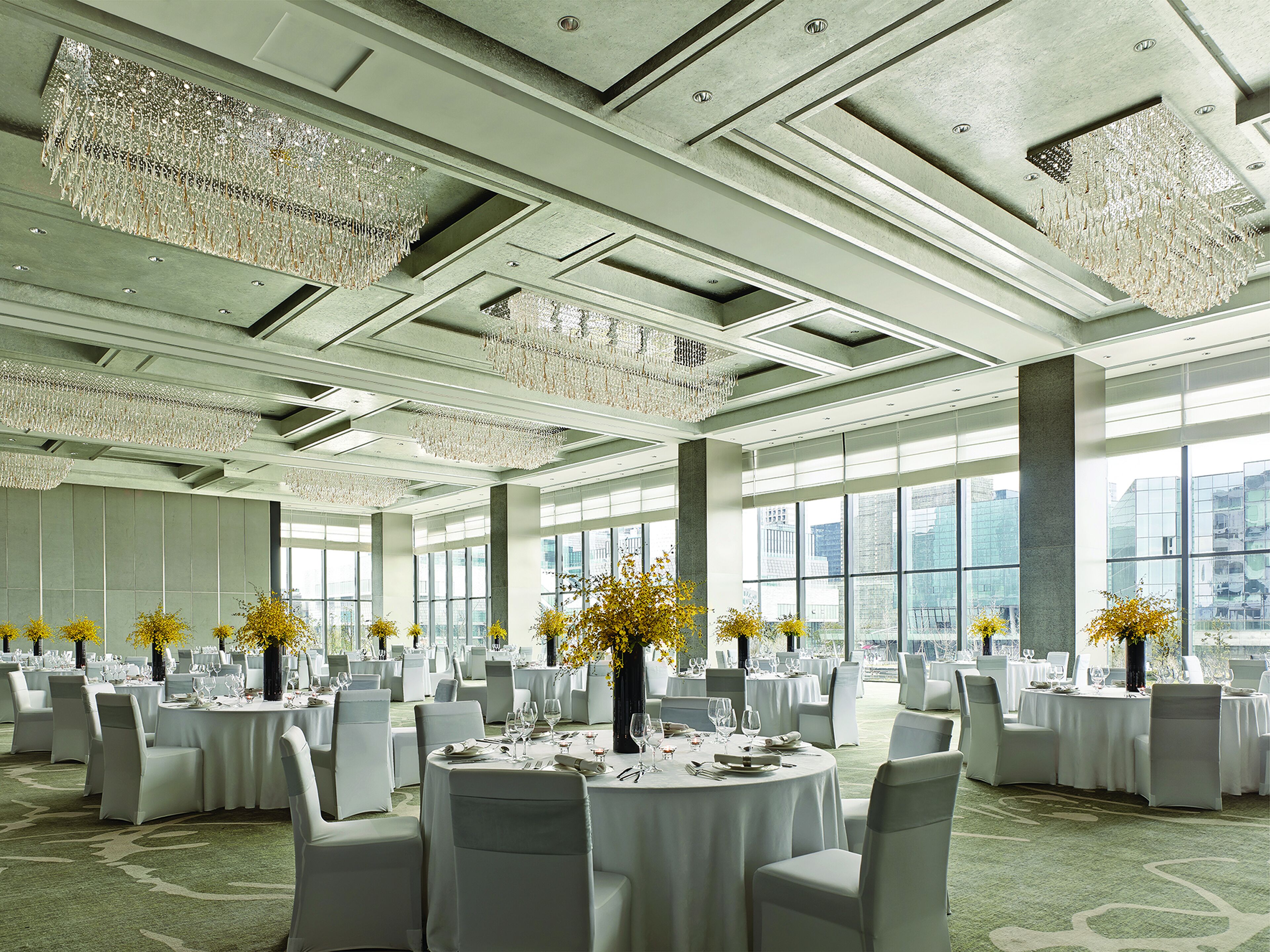 Une salle de banquet spacieuse, avec des tables rondes, des chaises blanches et des lustres.