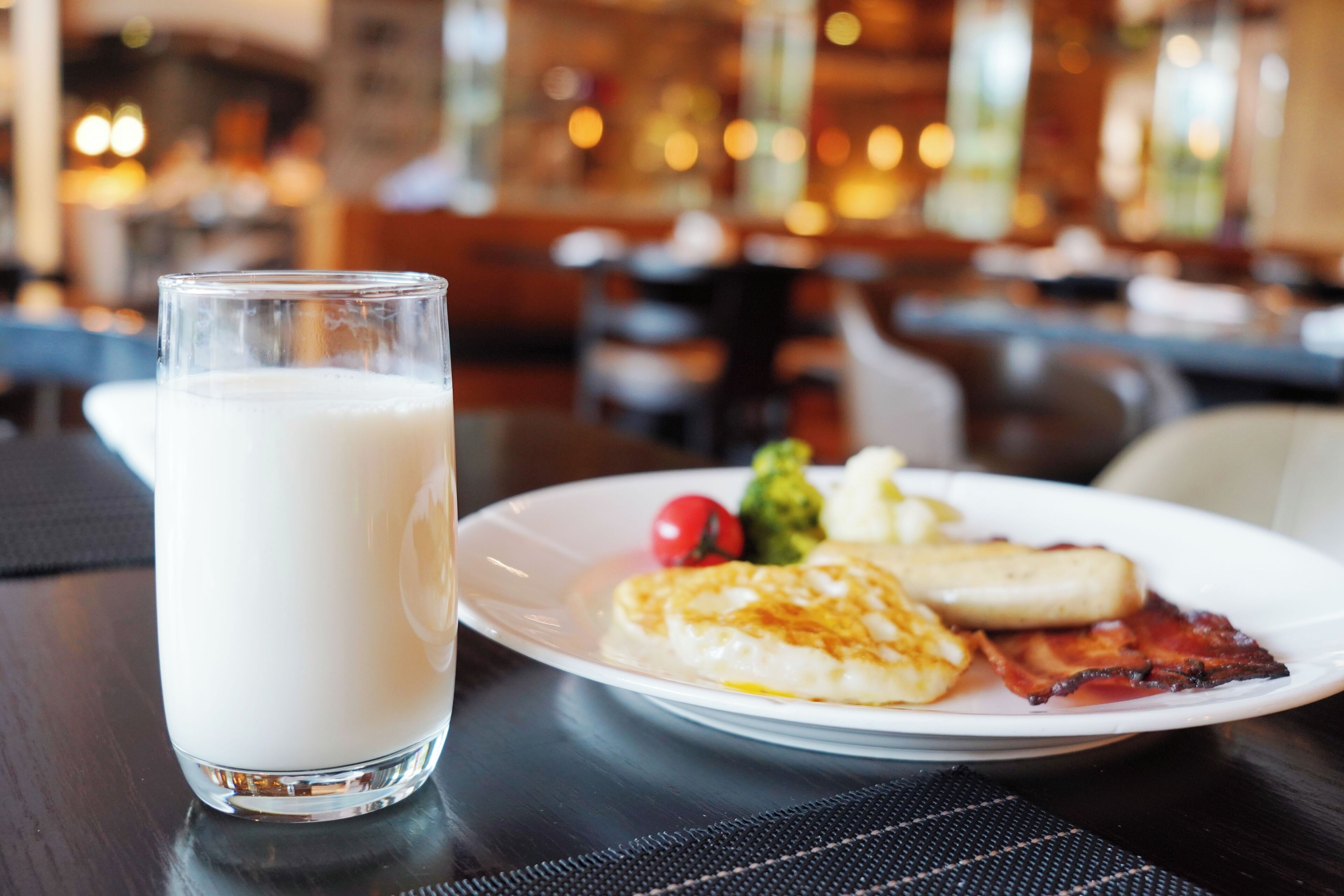 A breakfast setting with a glass of milk, eggs, bacon, and a small salad on a plate.