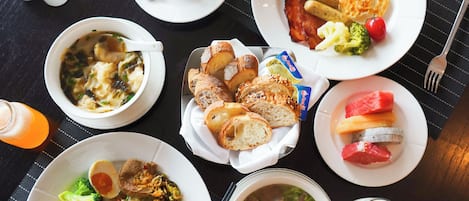Una mesa con diferentes platos de desayuno, como huevos, tostadas, sopa y fruta.