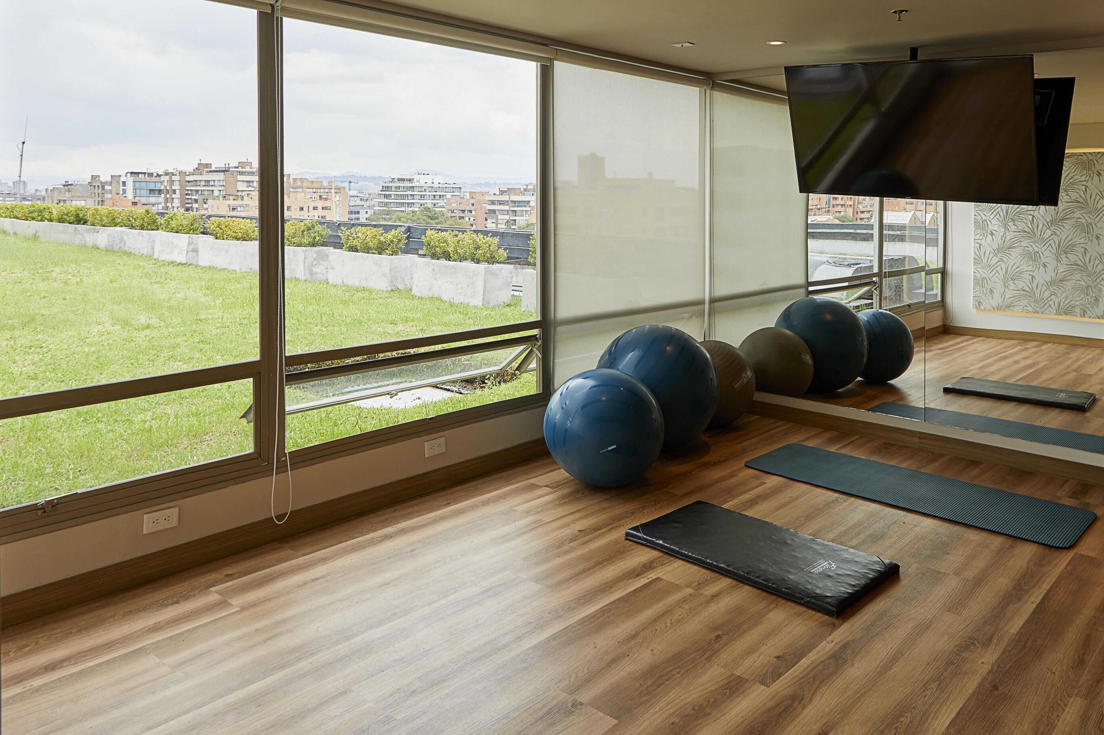 A gym with exercise balls, mats, and a TV on the wall.