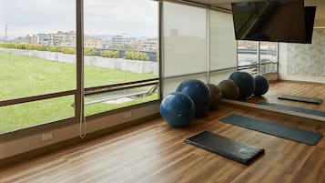 A gym with exercise balls, mats, and a TV on the wall.