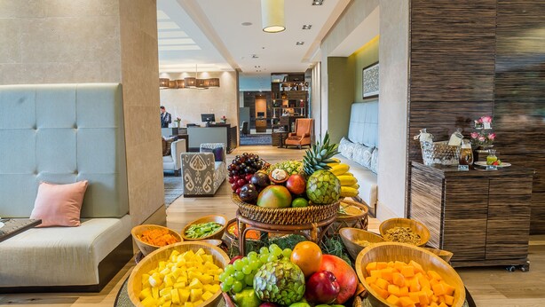 A buffet table with various fruits and a modern interior with a sofa and a reception desk. - EK Hotel By Preferred Hotels Group (Bogotá)