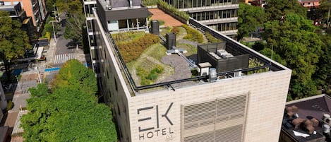 A hotel rooftop with a garden, modern architecture, and a view of the surrounding cityscape.