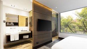 A modern bathroom with a large mirror, a flat-screen TV, and a large window offering a view of trees. - EK Hotel By Preferred Hotels Group (Bogotá)