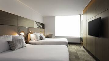 A modern hotel room with two beds, a flat-screen TV, a large window, and a minimalist design.