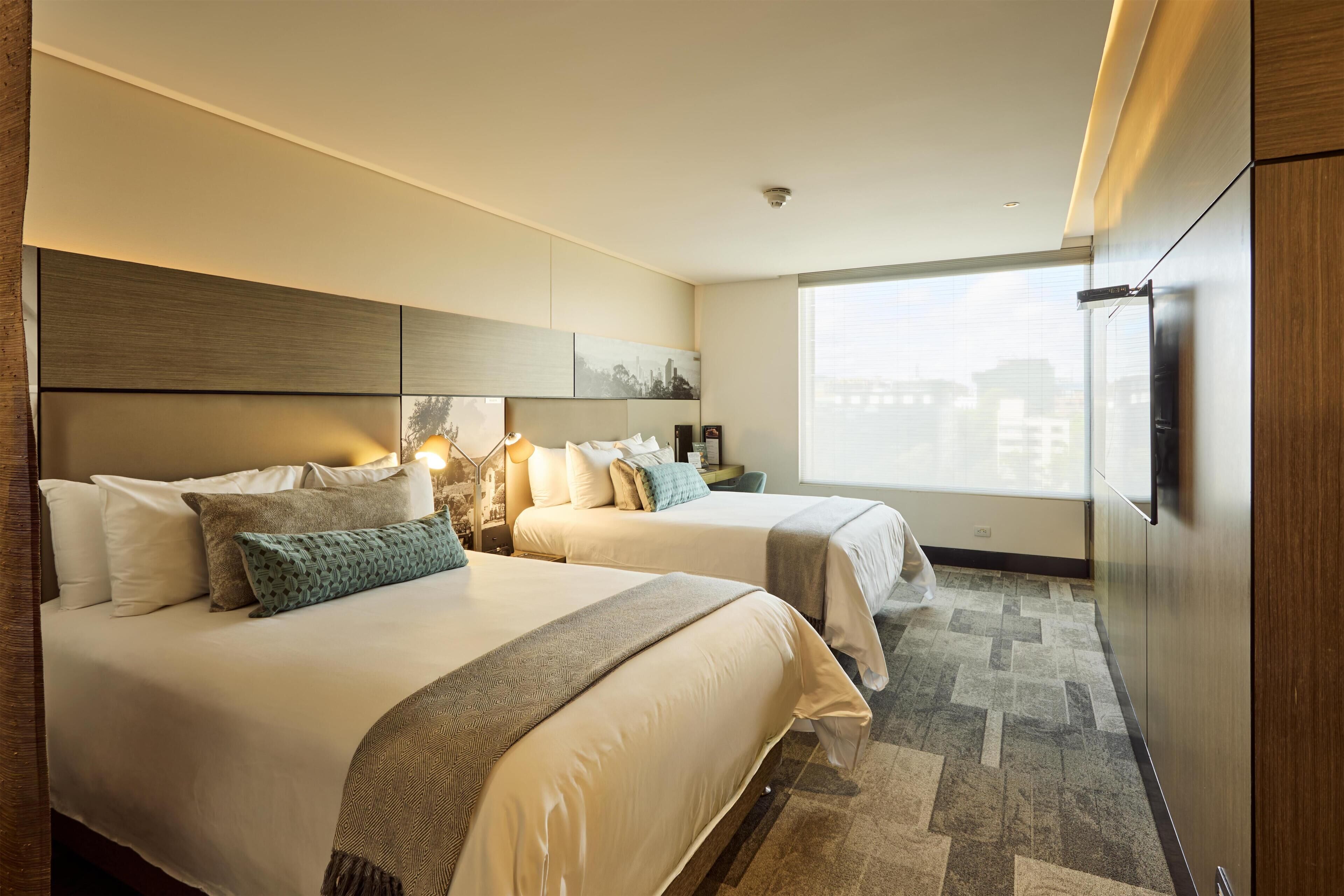 A hotel room with two beds, a large window, and a flat-screen TV.