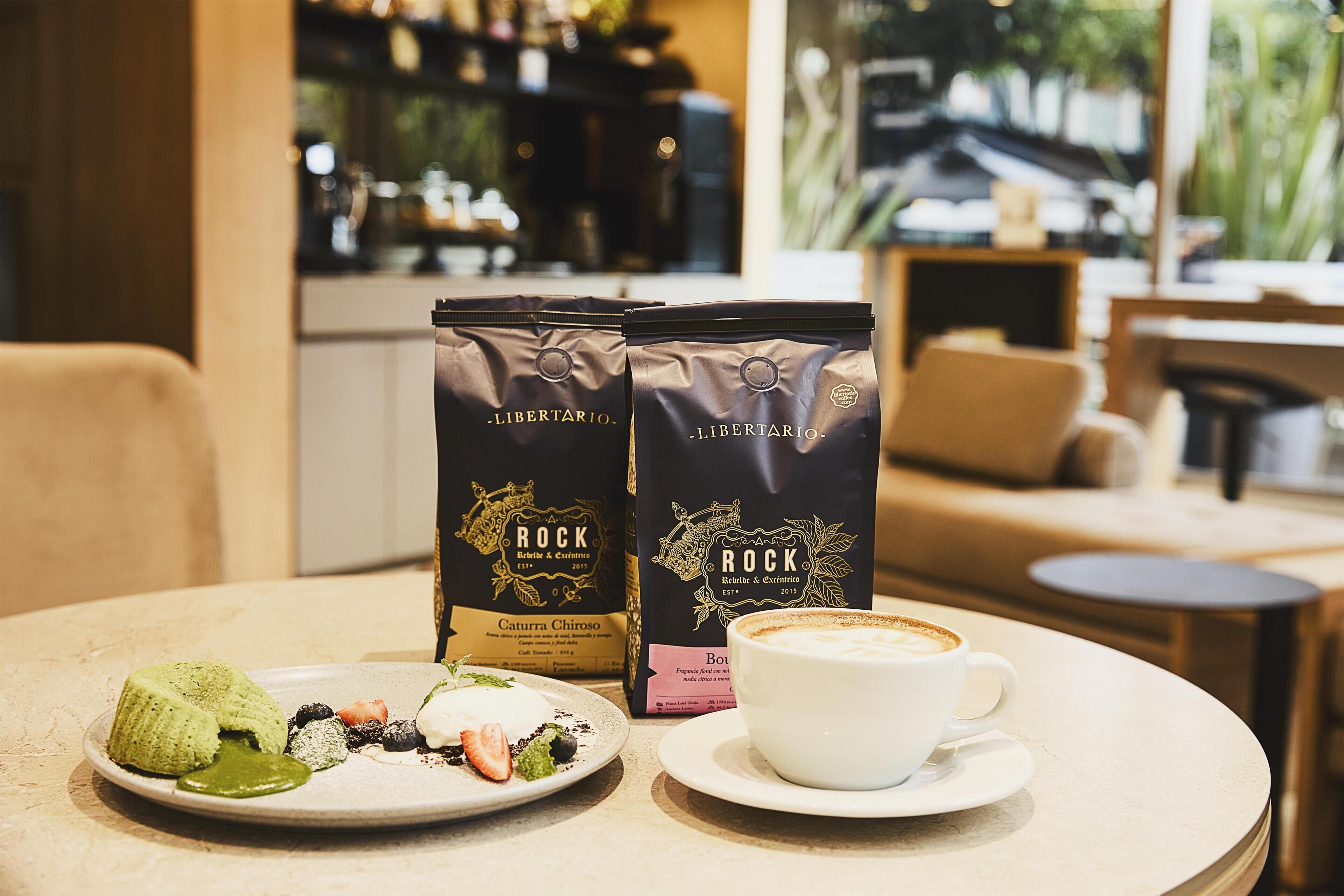 Une table avec une tasse de café, deux paquets de café et une assiette de nourriture.