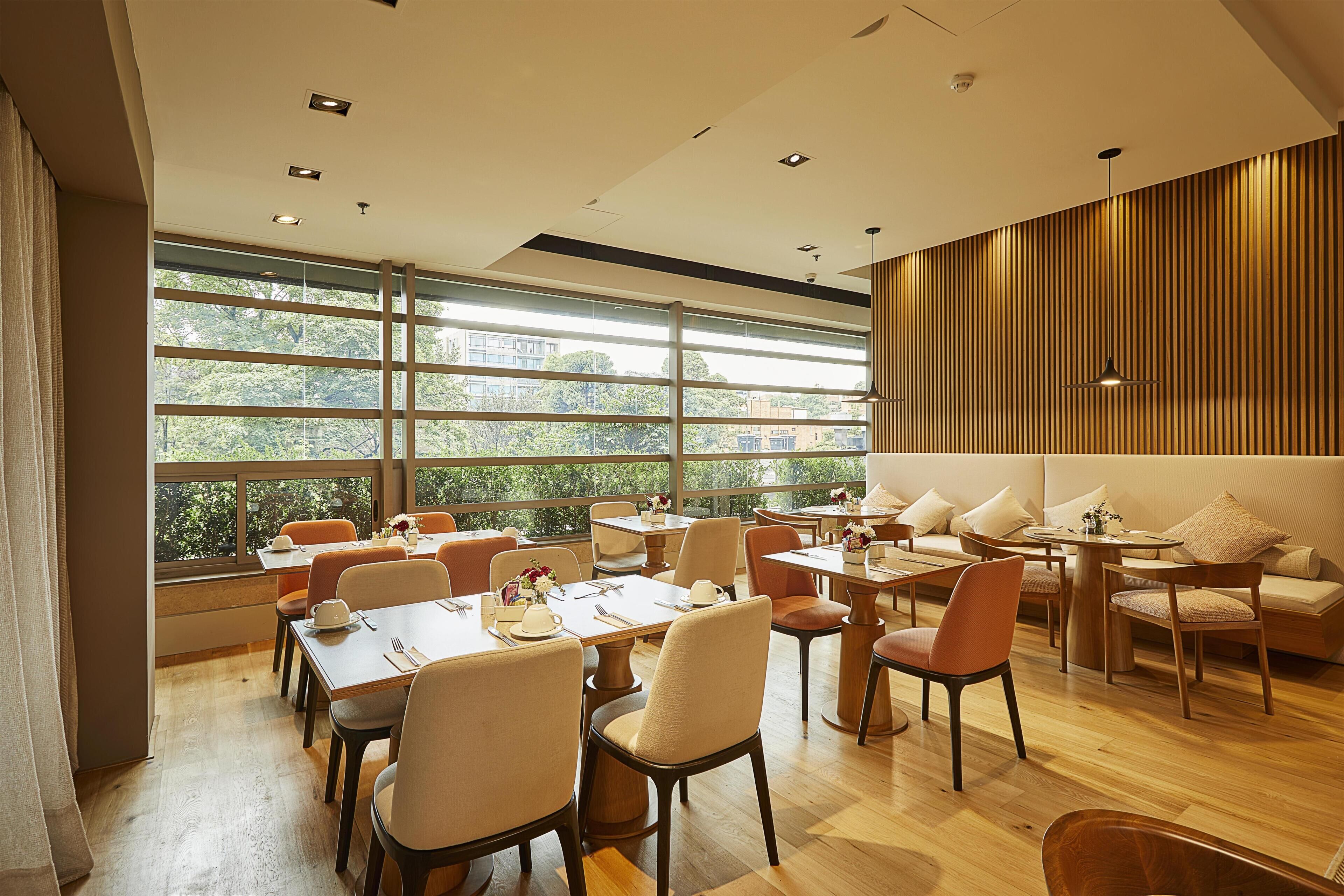 A modern dining area with large windows, wooden flooring, and a mix of tables and chairs.