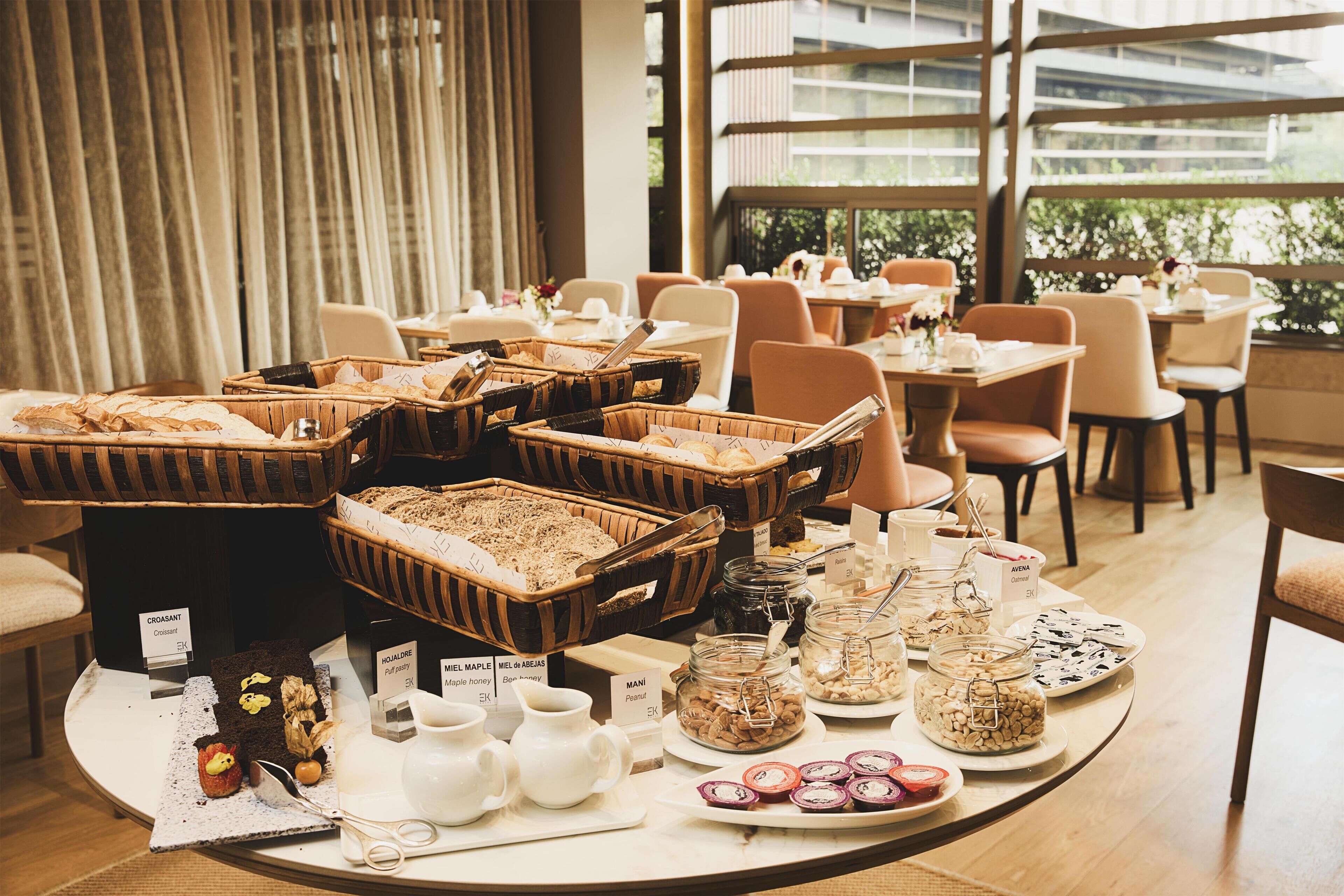A buffet setup with various food items and beverages, arranged on a round table in a well-lit room with large windows.