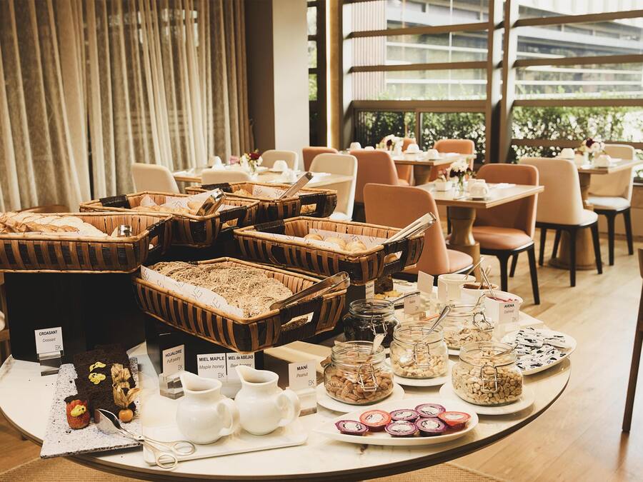 A buffet setup with various food items and beverages, arranged on a round table in a well-lit room with large windows.