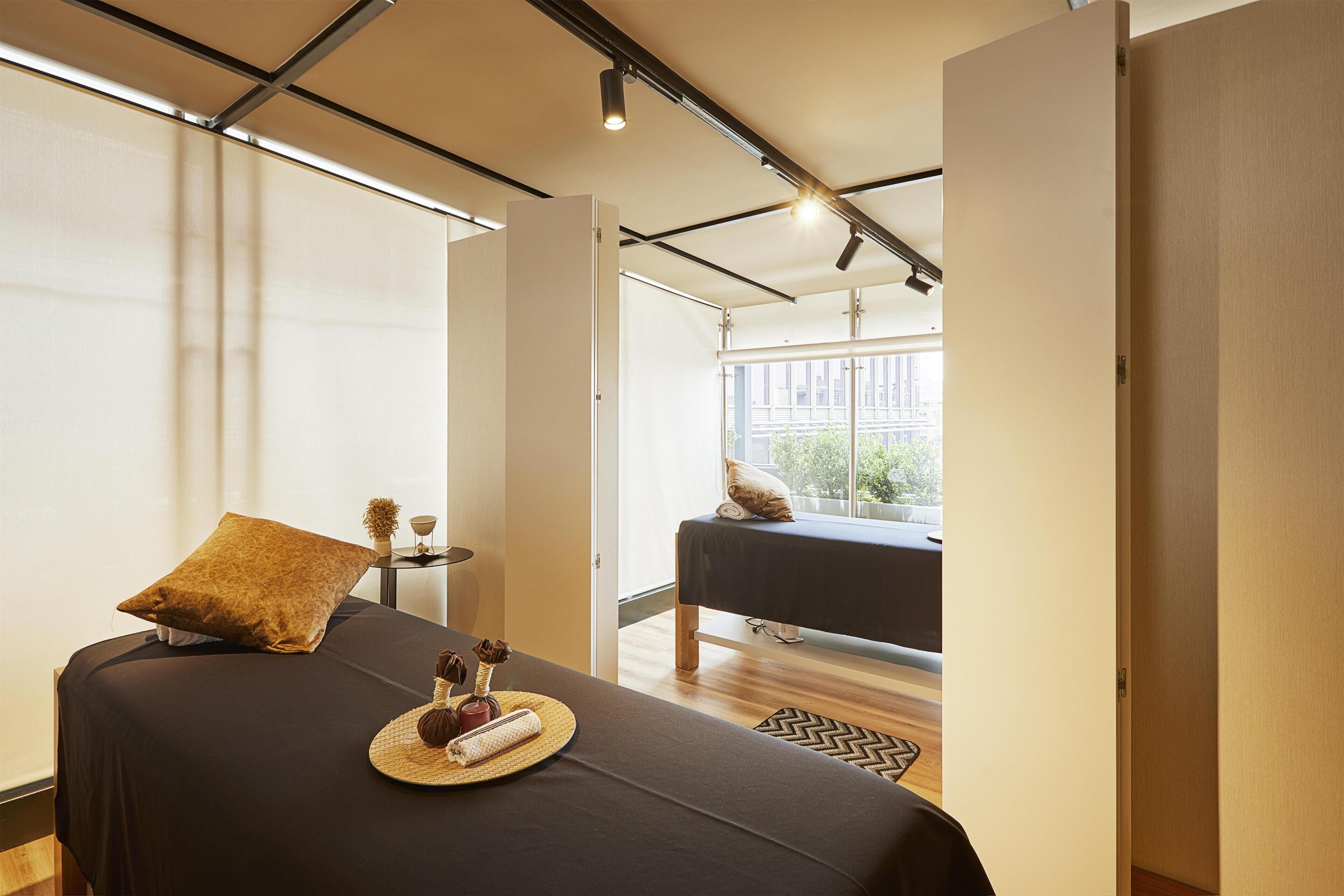 A modern room with a massage table, a small table with a tray, and a view of the outside.