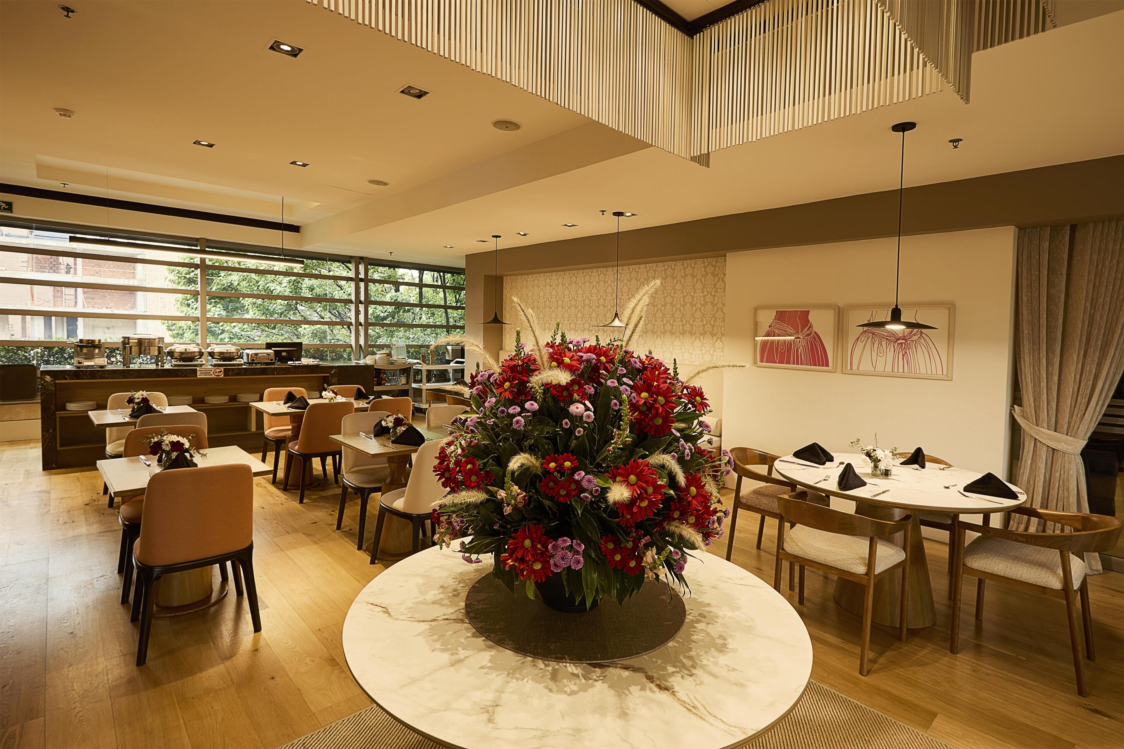 A modern dining area with round tables, chairs, and a central floral arrangement.