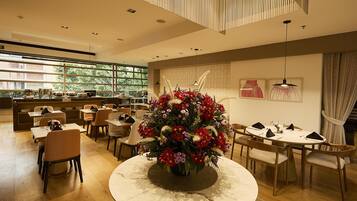 A modern dining area with round tables, chairs, and a central floral arrangement.