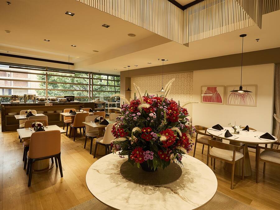 A modern dining area with round tables, chairs, and a central floral arrangement.