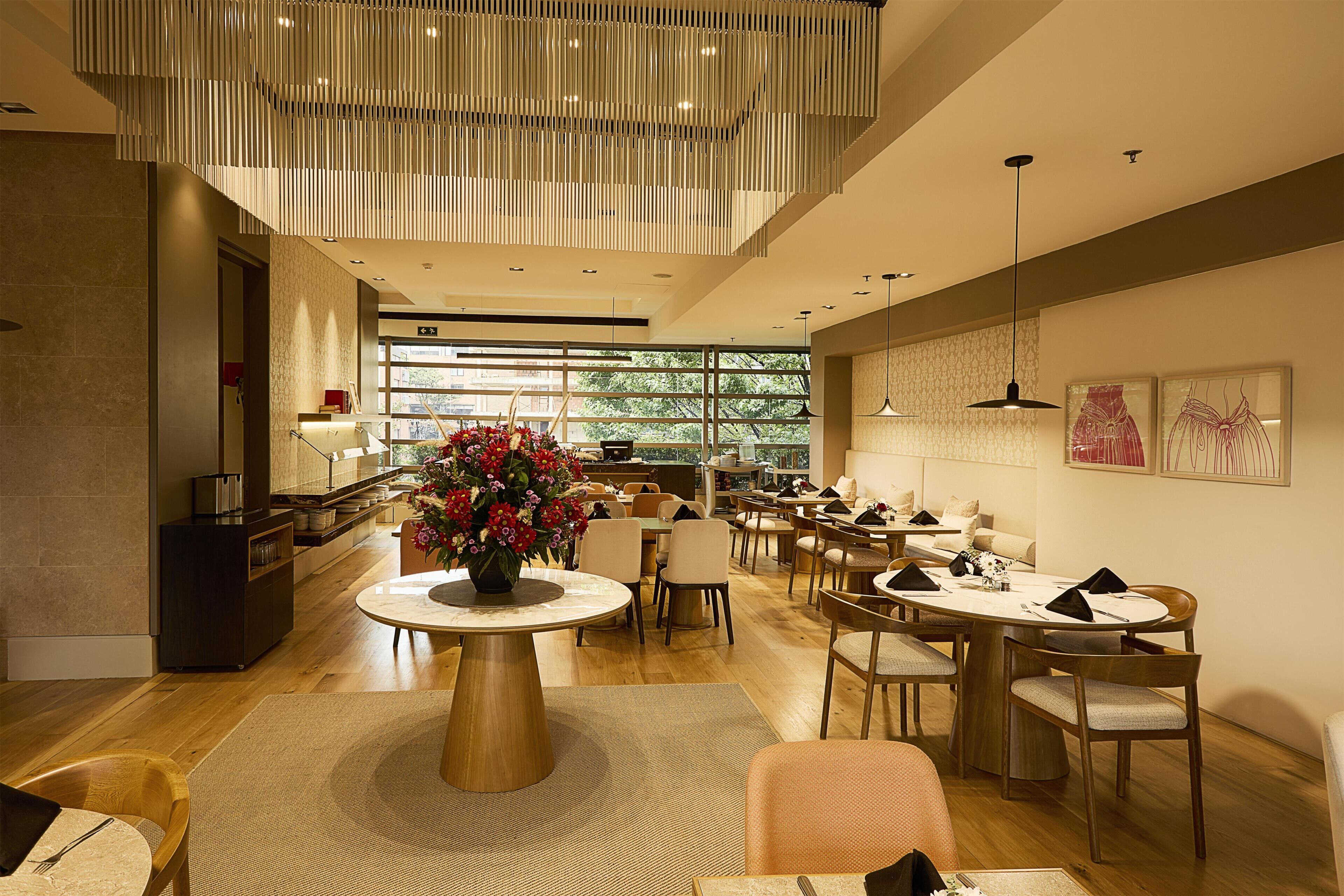 A modern dining area with a central round table, multiple chairs, a decorative vase, and a contemporary ceiling light fixture.