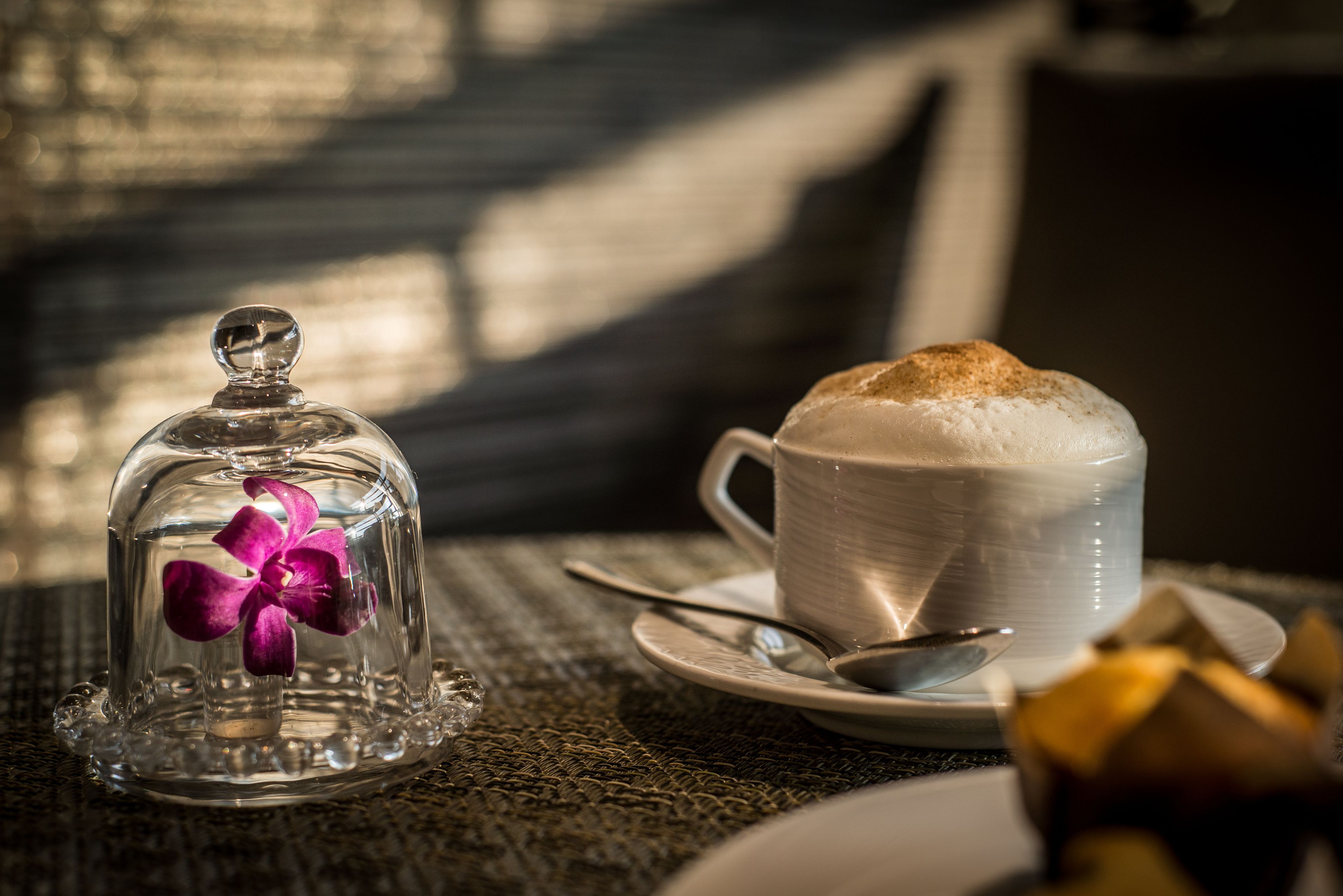 Una mesa con una taza de café, una cloche con una flor y una cuchara.