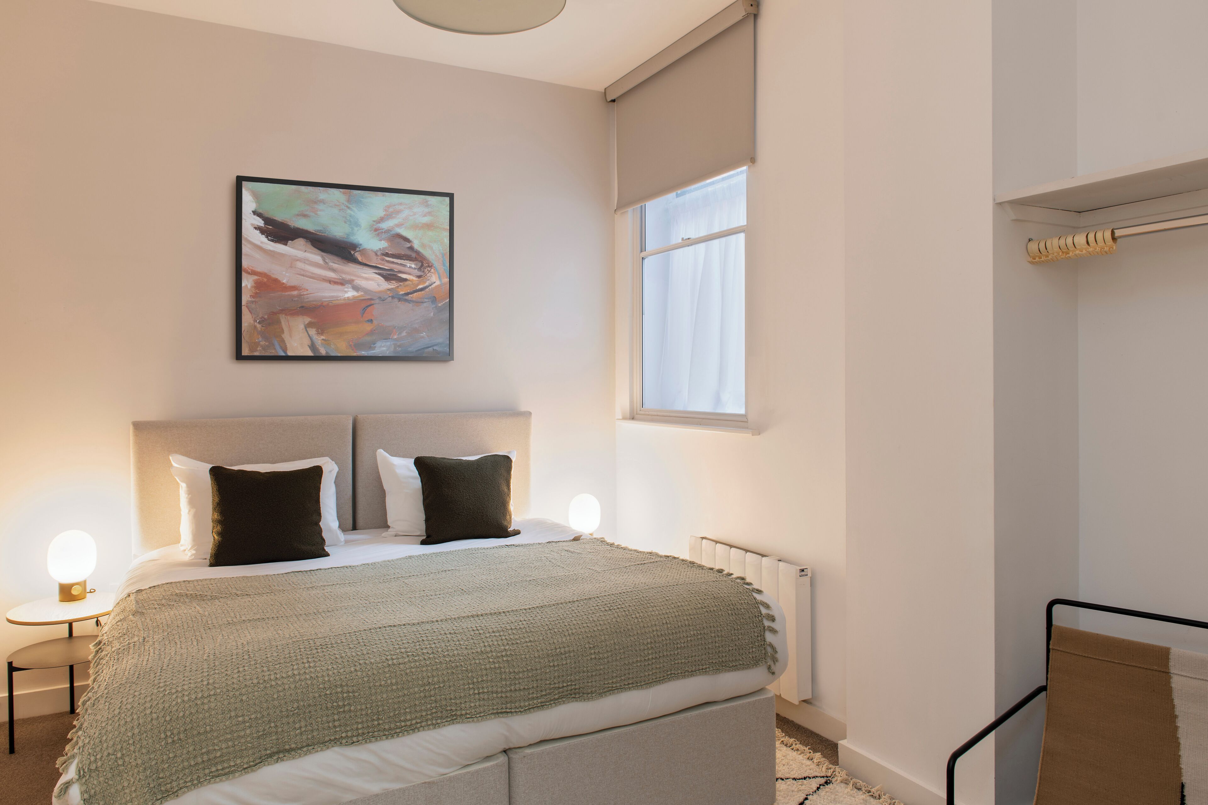 A modern bedroom with a large bed, a painting, a window, and a radiator.