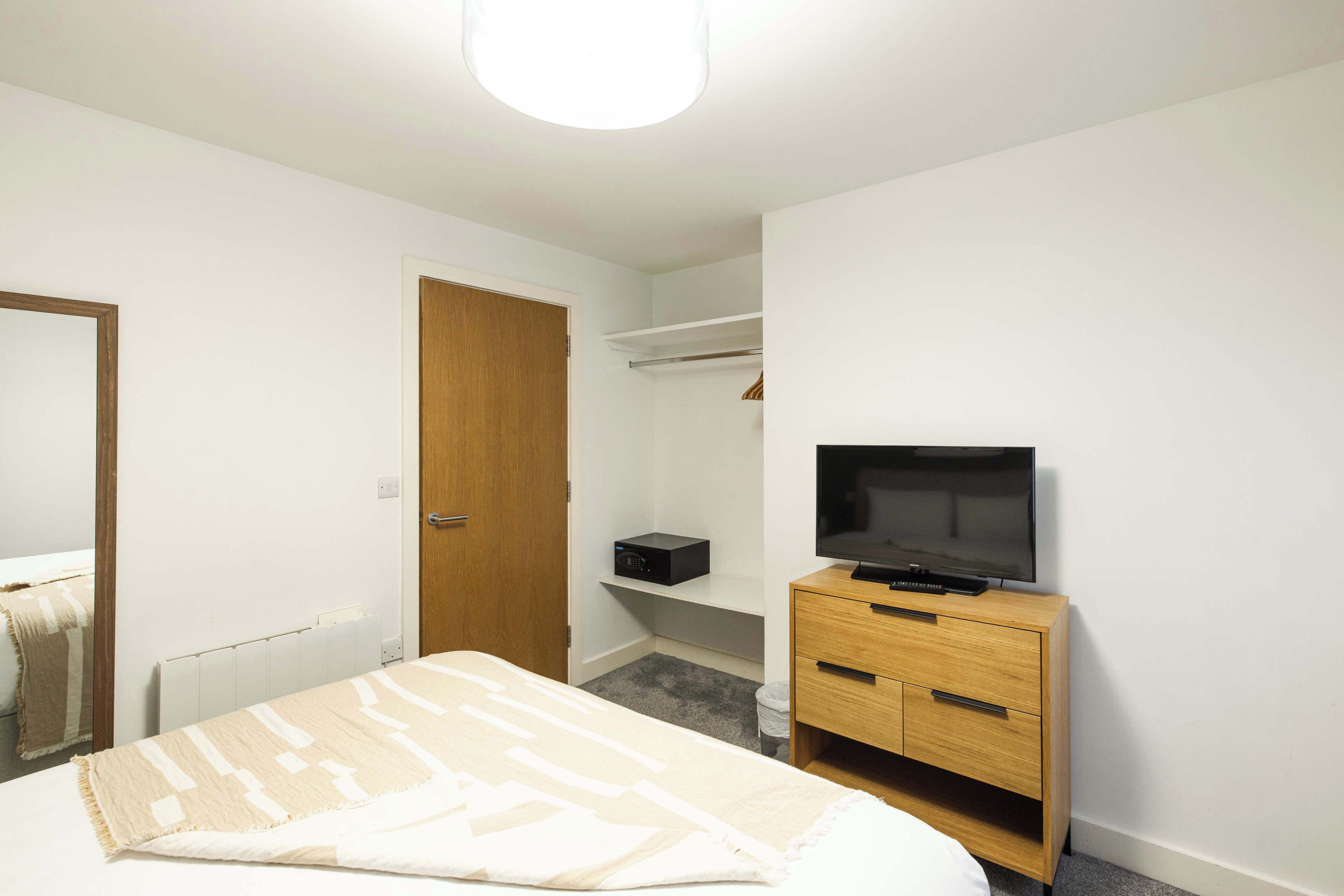 A bedroom with a bed, a wooden dresser, a television, a wardrobe, and a mirror.