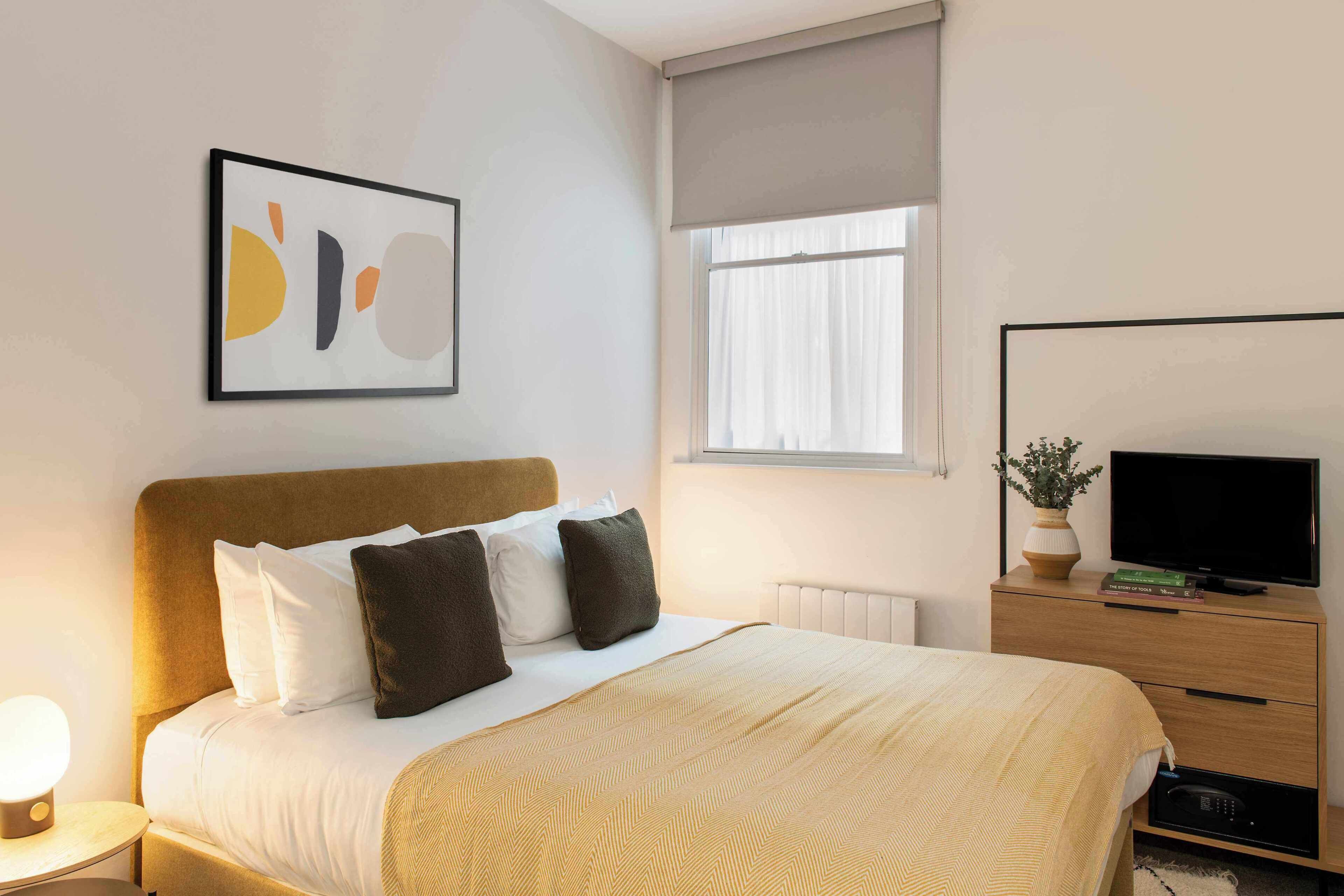Ein Hotelzimmer mit Bett, Nachttisch, Fernseher und einem Fenster mit Vorhängen.