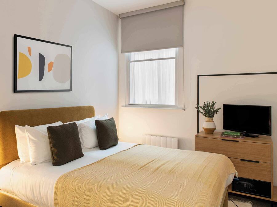 A hotel room with a bed, bedside table, TV, and a window with curtains.