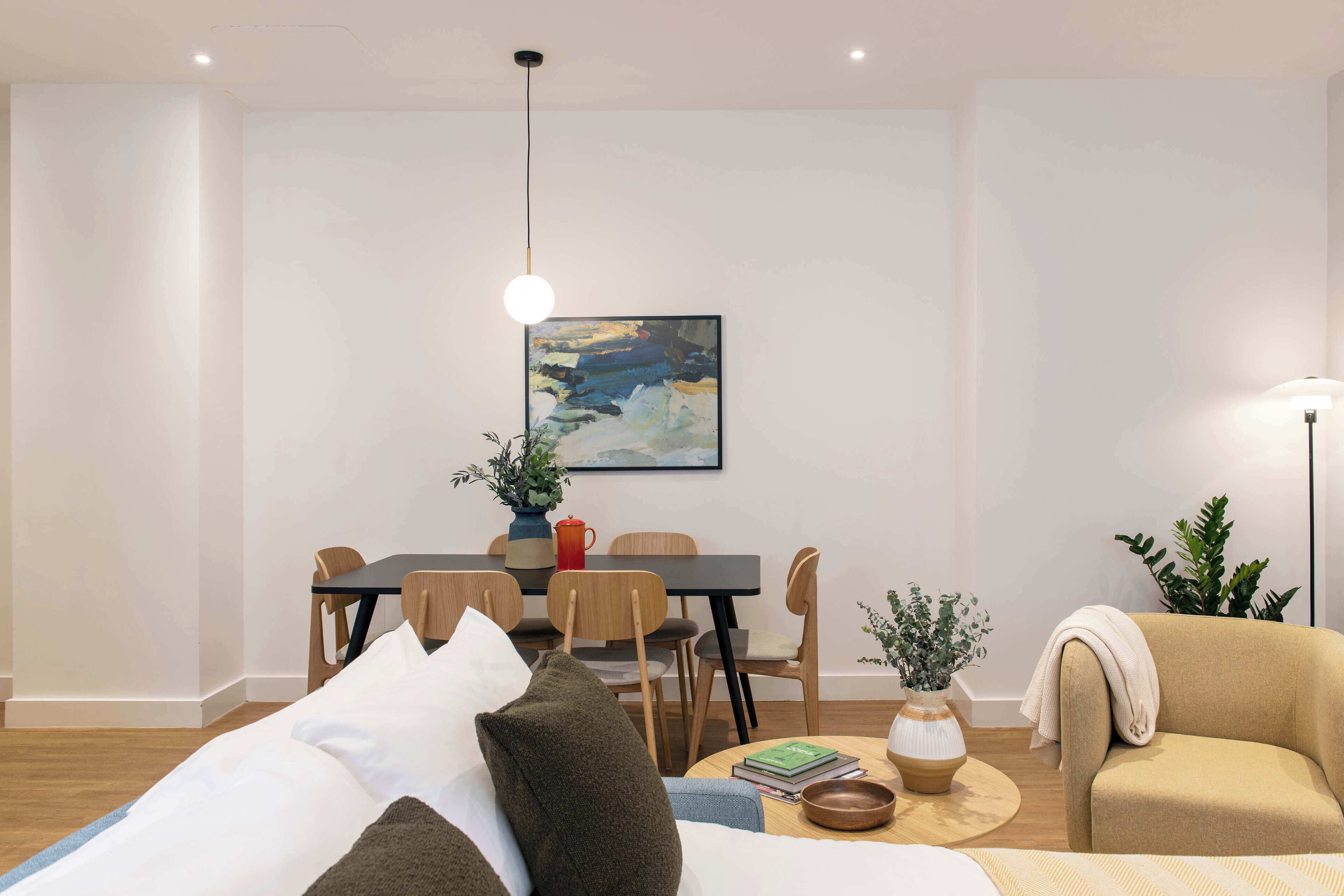 A modern living room with a sofa, a dining area with a table and chairs, and a painting on the wall.