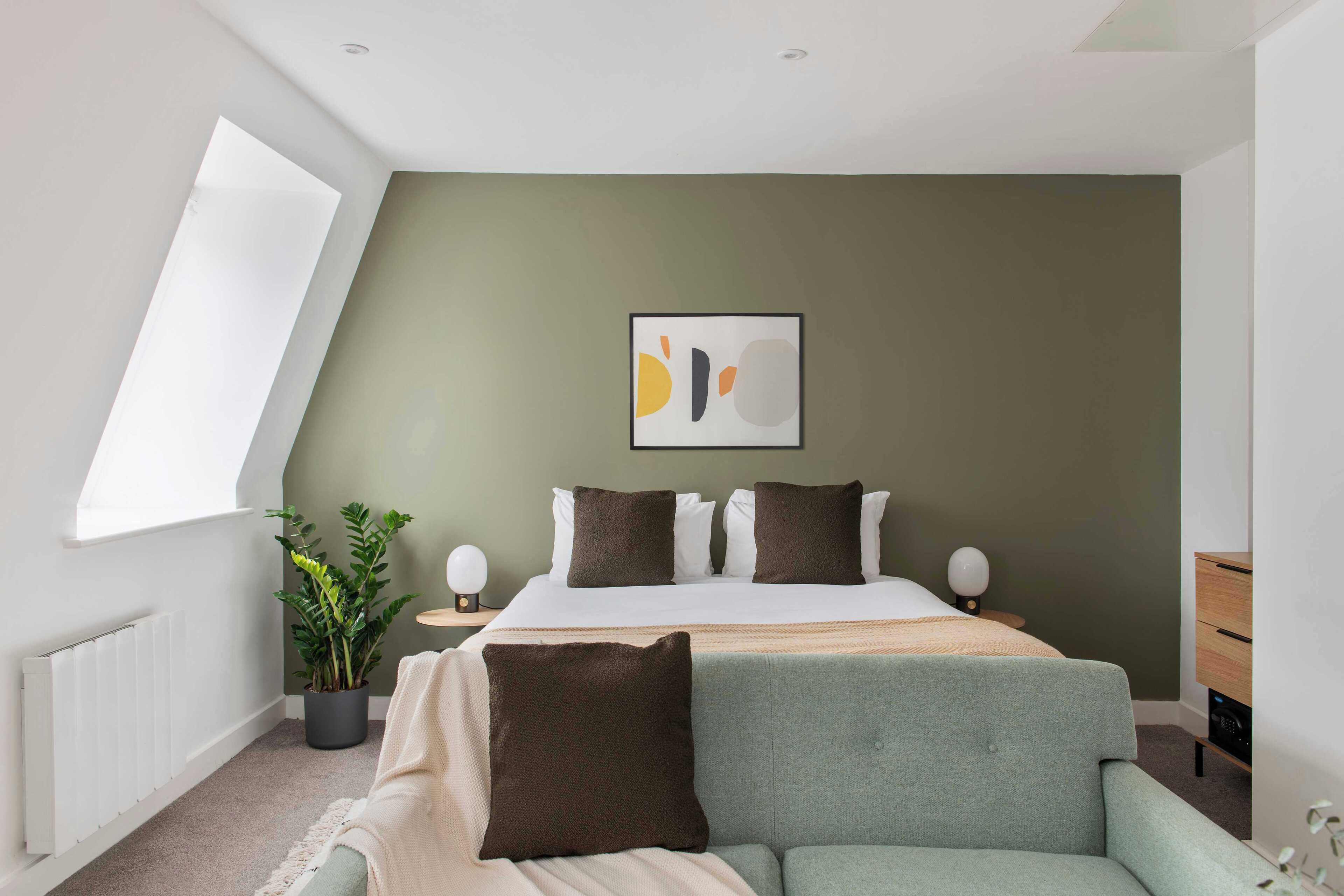 Un dormitorio moderno con una cama, una planta en maceta, una mesita de noche con lámpara y vistas al exterior.