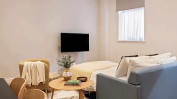 Une chambre d’hôtel moderne équipée d’un téléviseur à écran plat, d’un canapé, d’un fauteuil, d’une petite table ronde avec des livres et d’une fenêtre avec des rideaux.