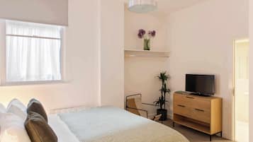 A bedroom with a bed, a TV on a wooden dresser, a chair, and a potted plant.