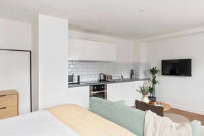 A modern kitchen with white cabinets, a microwave, toaster, and a kettle. There is a TV mounted on the wall and a plant on the counter. - Cove Minshull Street (Manchester)