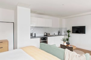 Una cocina moderna con armarios blancos, microondas, tostadora y hervidor. Hay un televisor montado en la pared y una planta sobre la encimera.