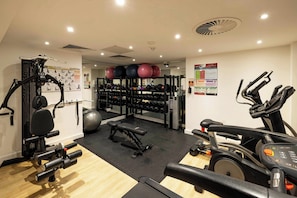 Un gimnasio con equipo de ejercicio, una banca y una pared con carteles informativos.