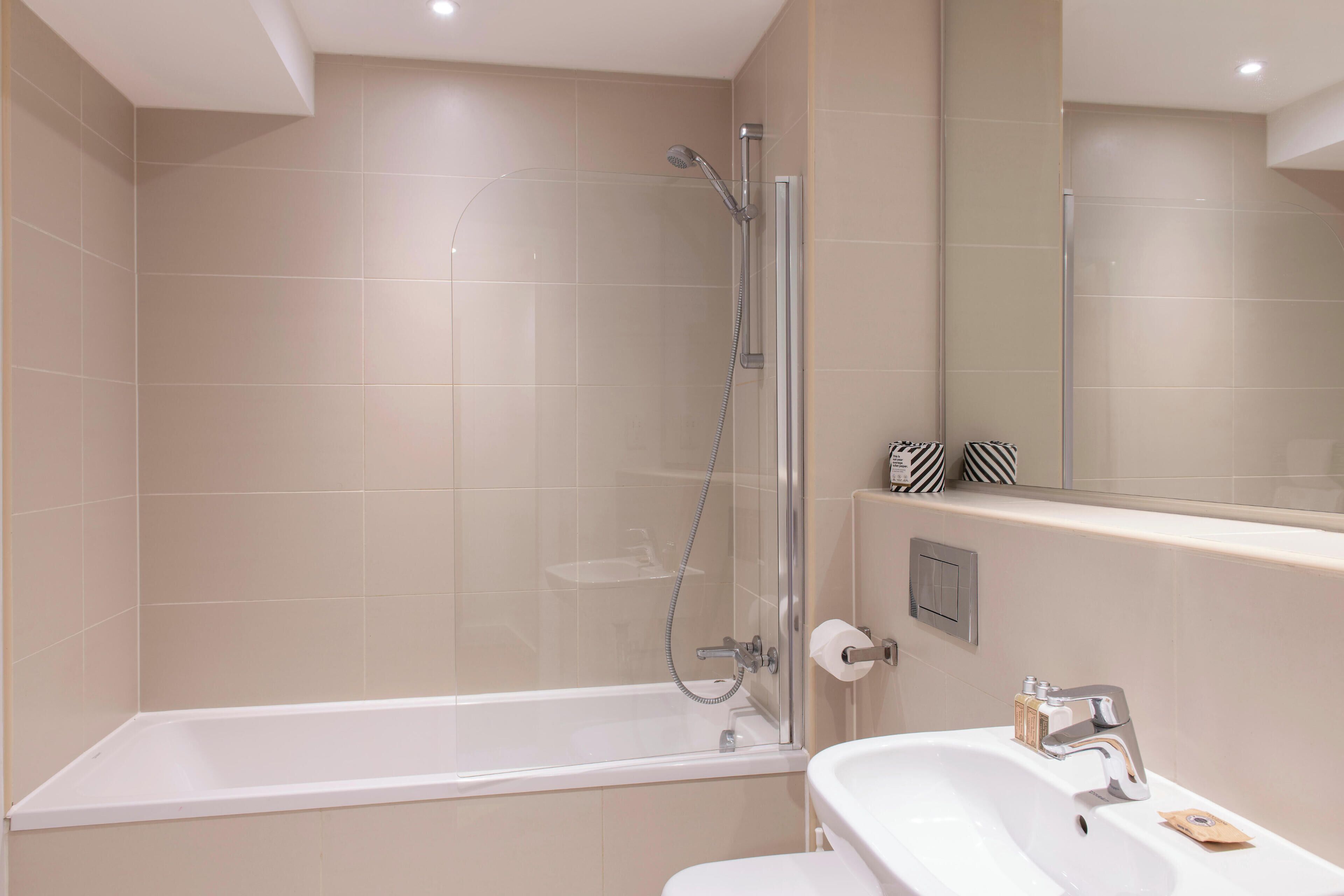 Ein modernes Badezimmer mit einer gläsernen Duschkabine, einer weißen Badewanne und einem Waschbecken mit Spiegel darüber.