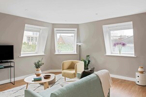 Una sala de estar moderna con televisor, sofá, sillón, mesa de centro y planta.