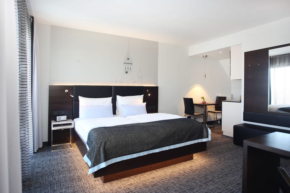 A modern hotel room with a large bed, bedside tables, a desk, and a chair.