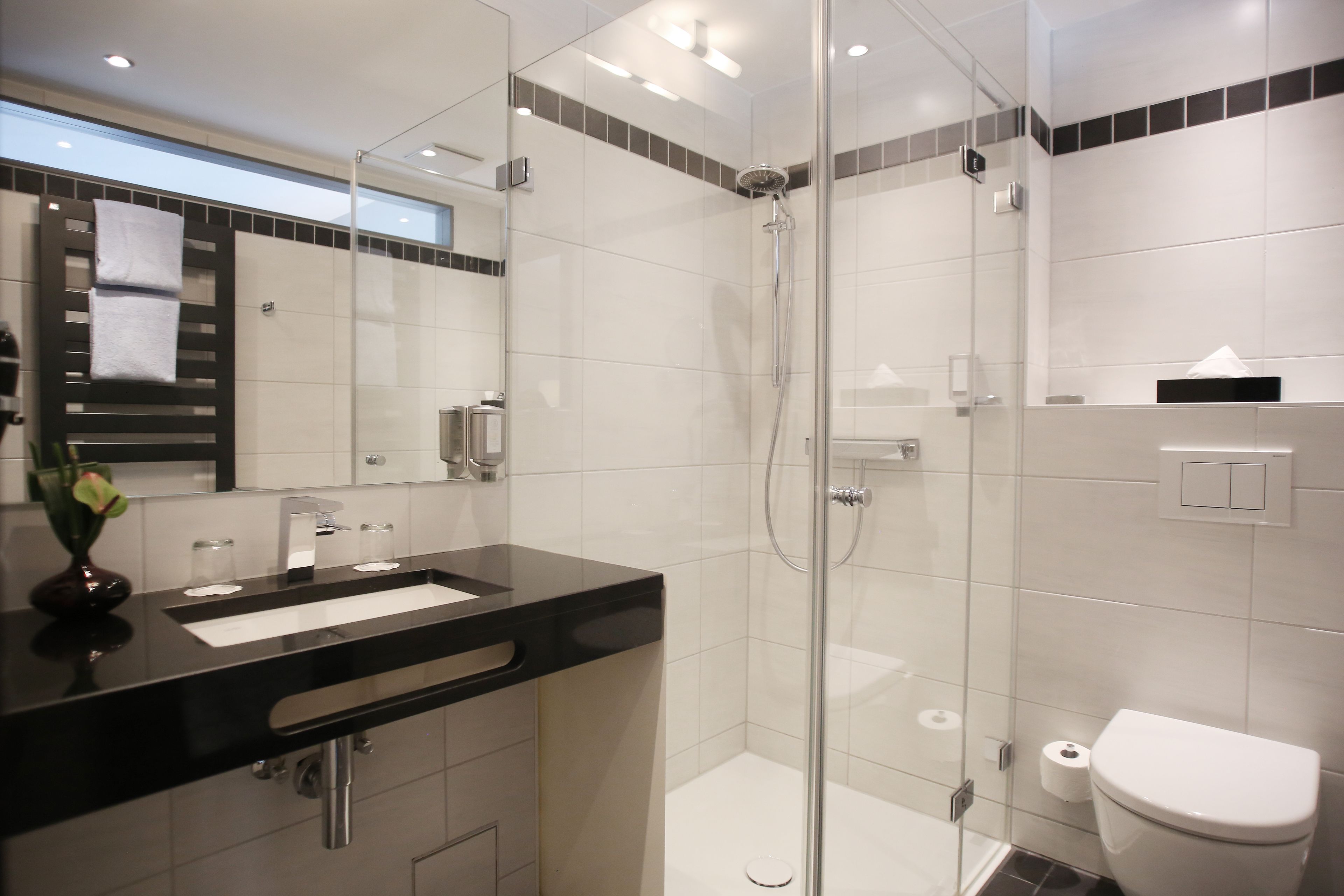 A modern bathroom with a glass-enclosed shower, a black countertop sink, and a white toilet.