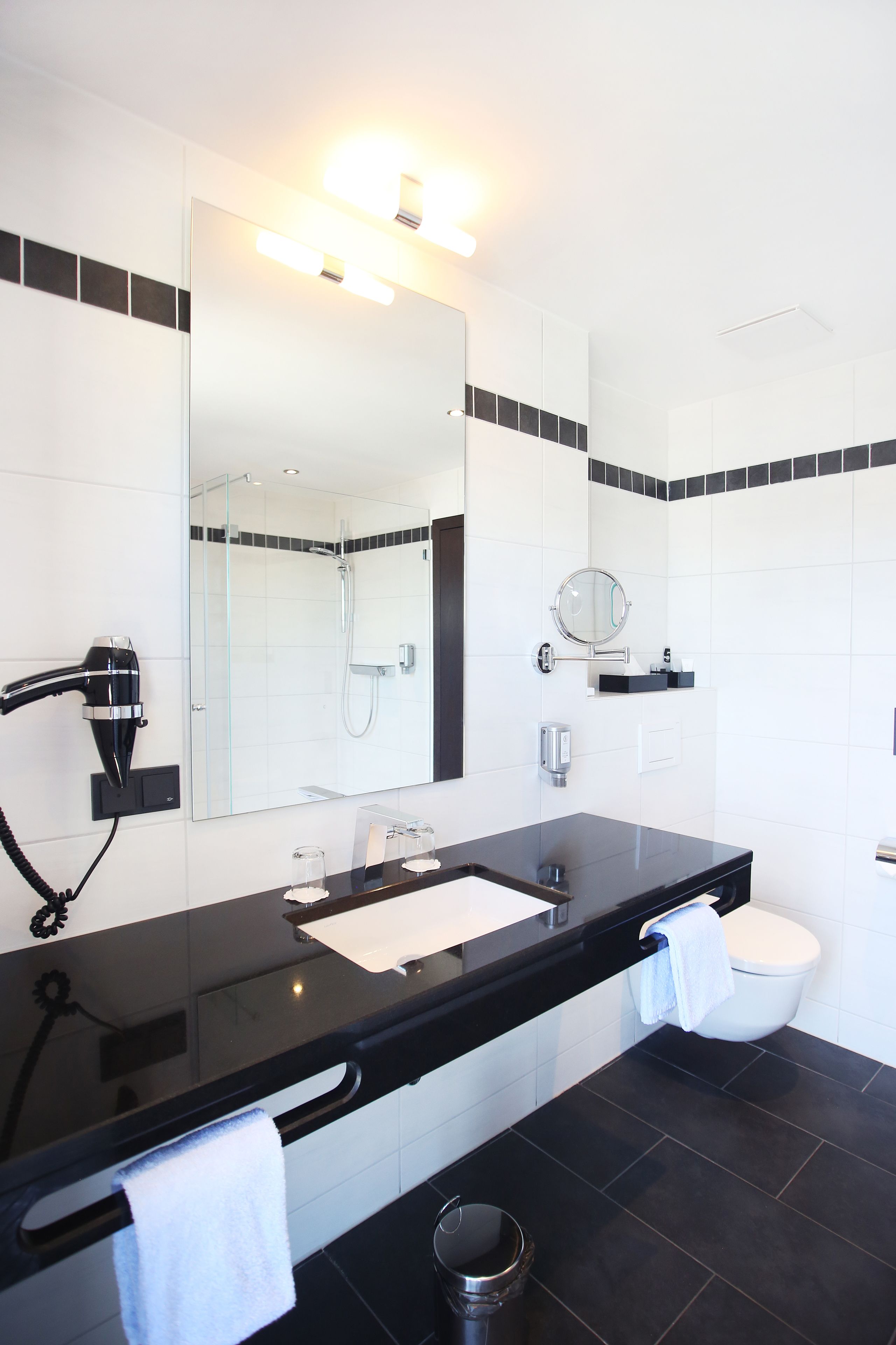 Un baño moderno con encimera negra, cabina de ducha de vidrio, lavabo blanco y retrete.
