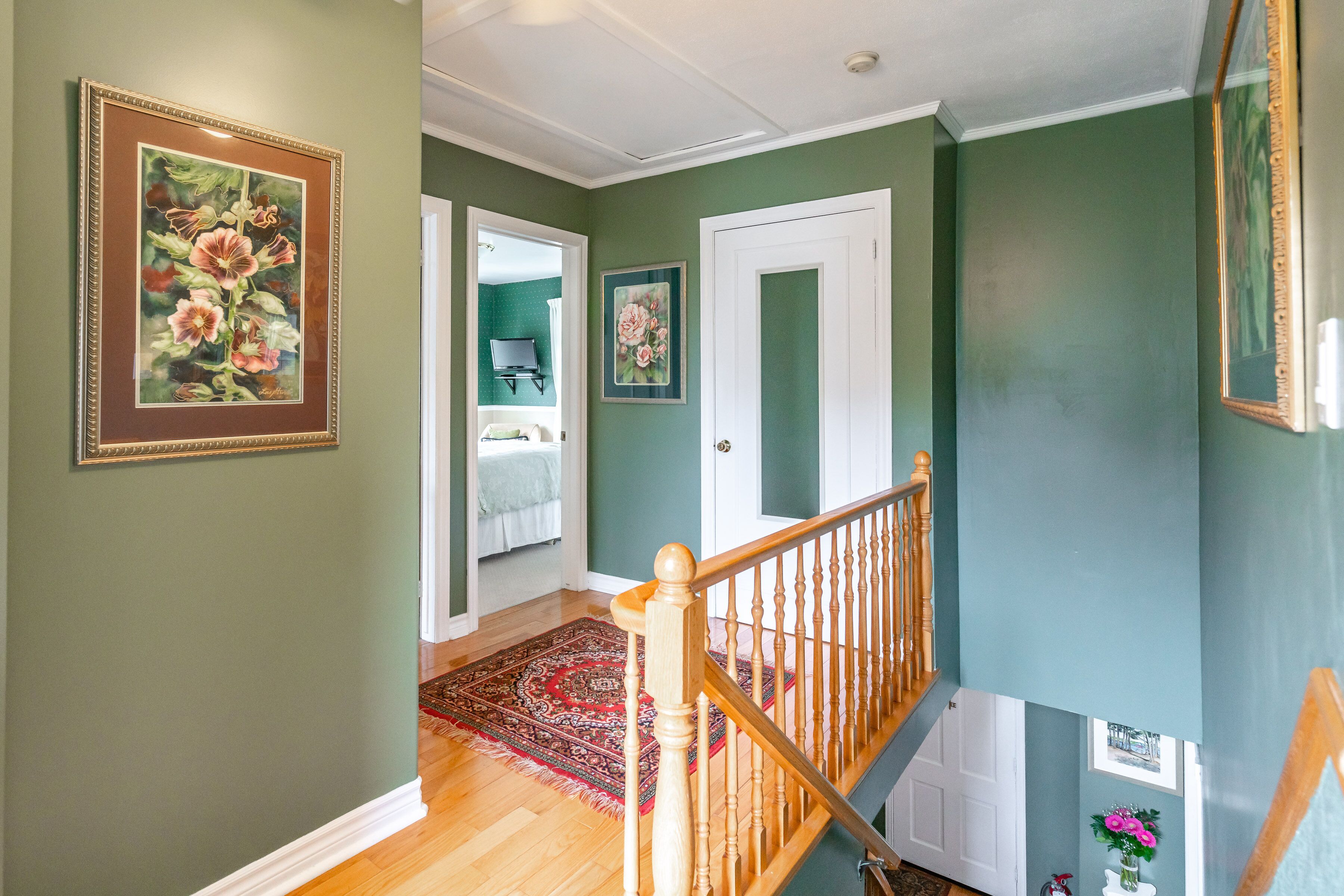 Un couloir aux murs verts, doté d’un plancher en bois et d’un escalier avec une rampe en bois.