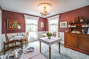 Uma sala de jantar com uma mesa posta para dois, um candelabro e um aparador com jogos de chá.