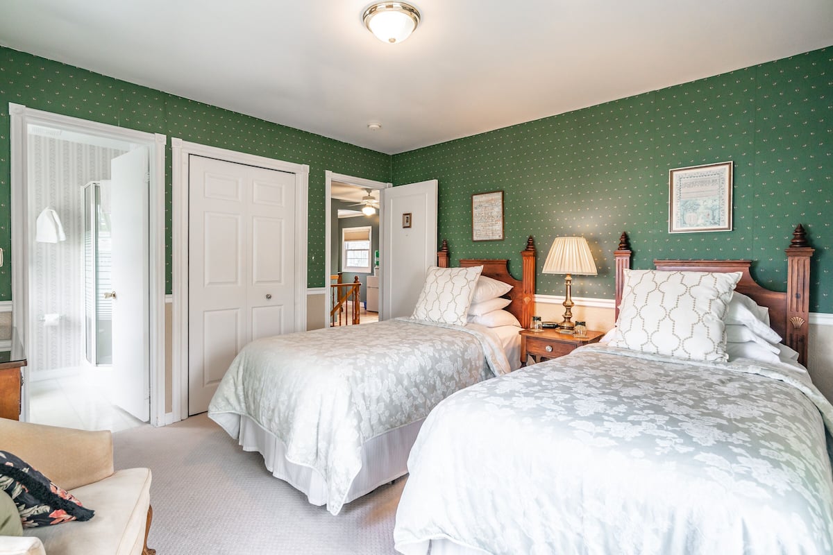 A bedroom with two beds, a nightstand, a chair, and a door leading to another room.