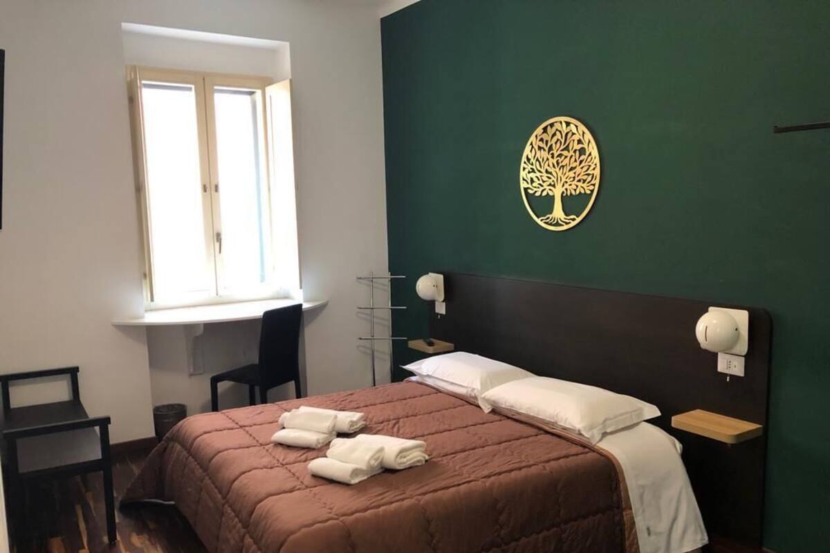 Un dormitorio con cama, escritorio, silla, ventana y decoración de árbol montada en la pared.