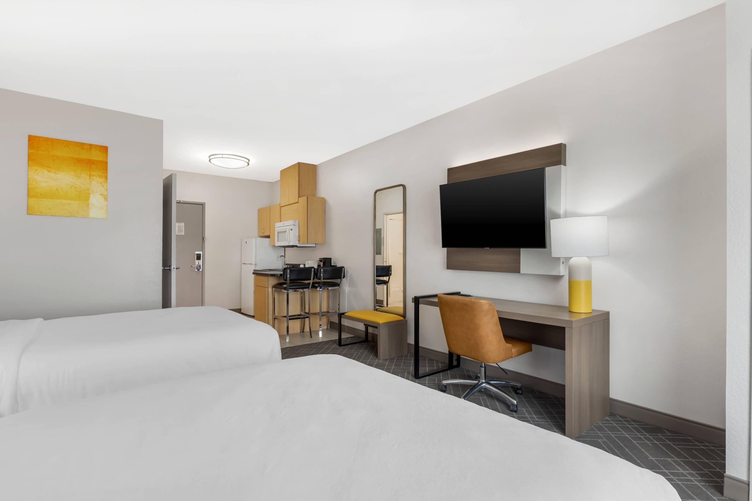 A hotel room with two beds, a desk with a chair, a TV, and a microwave.